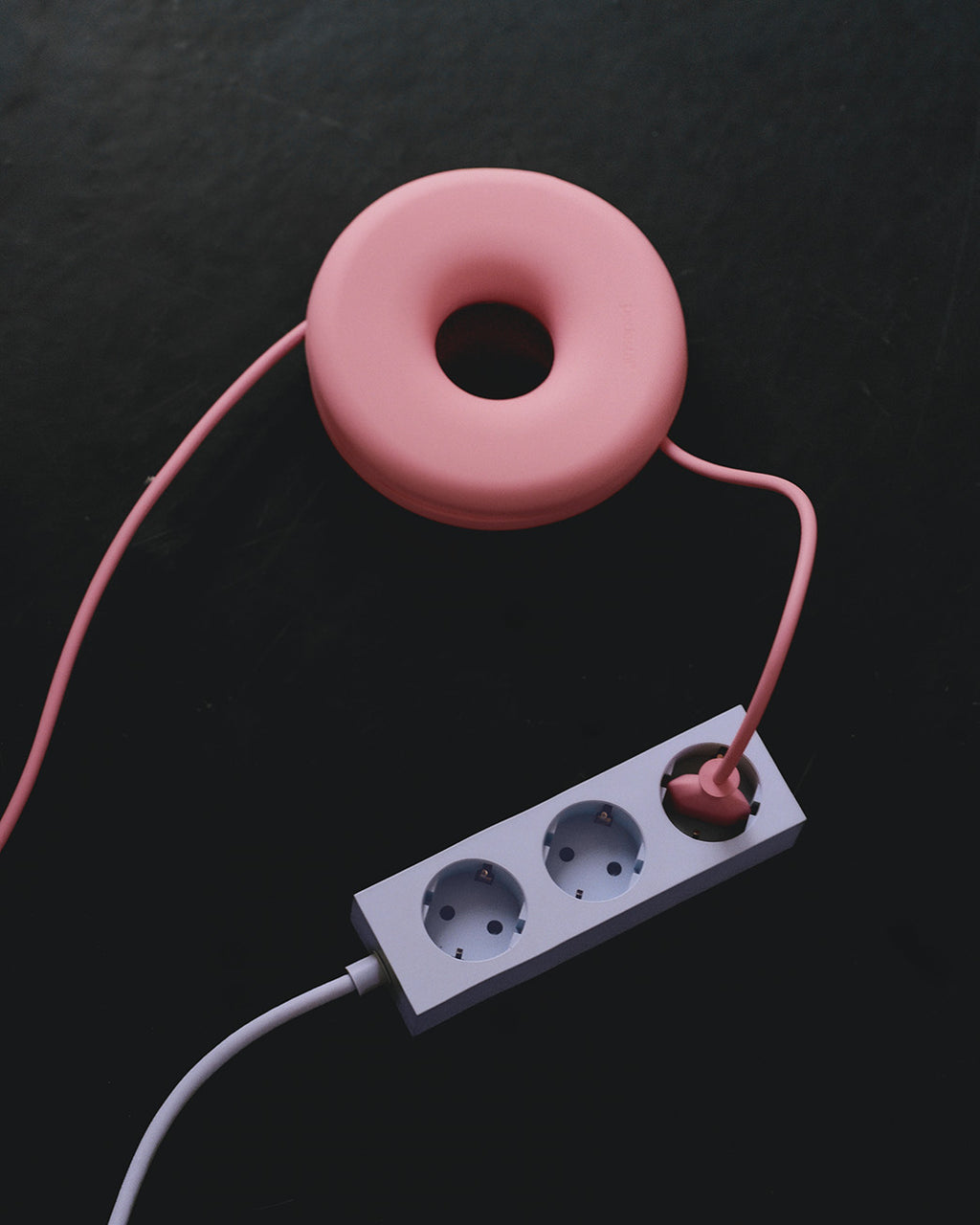 Cable Bagel in Bubble Gum coiling a pink cord on a dark surface, plugged into a white power strip