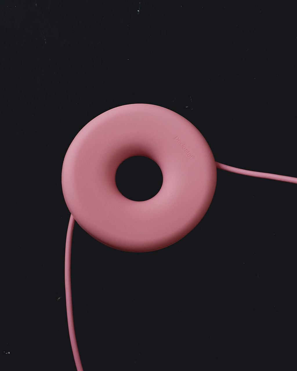 Cable Bagel in Bubble Gum studio packshot, pink donut-shaped cable manager on black with cord threaded through