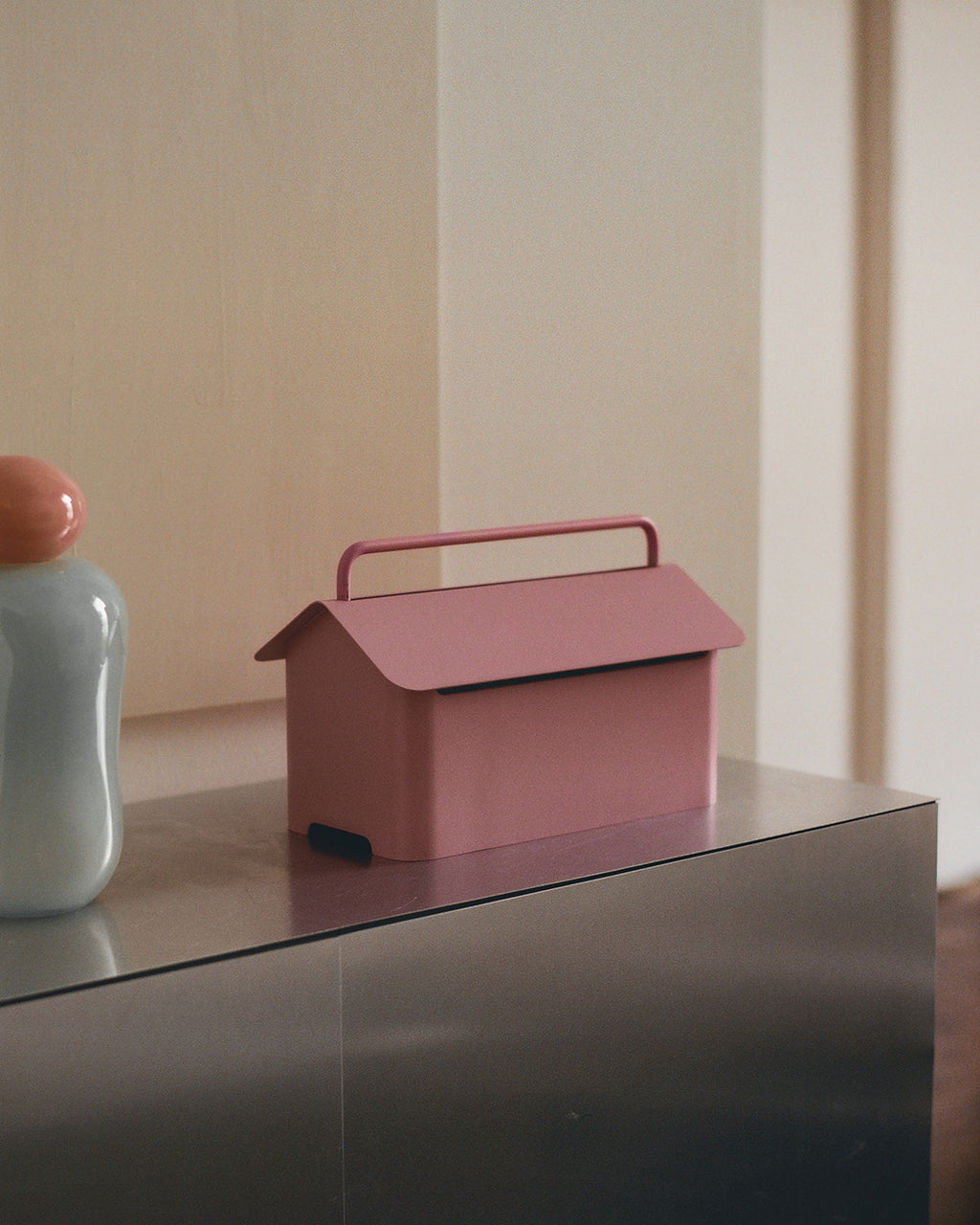 Cable Villa in Bubble Gum, house-shaped cable box with carry handle, styled on a steel sideboard beside a pale vase