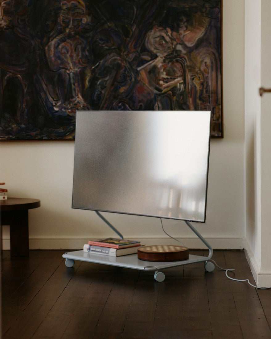 Disco stand in Powder Blue on wheels holding a flat-screen TV, books and a wood box, in a dark-floored living room