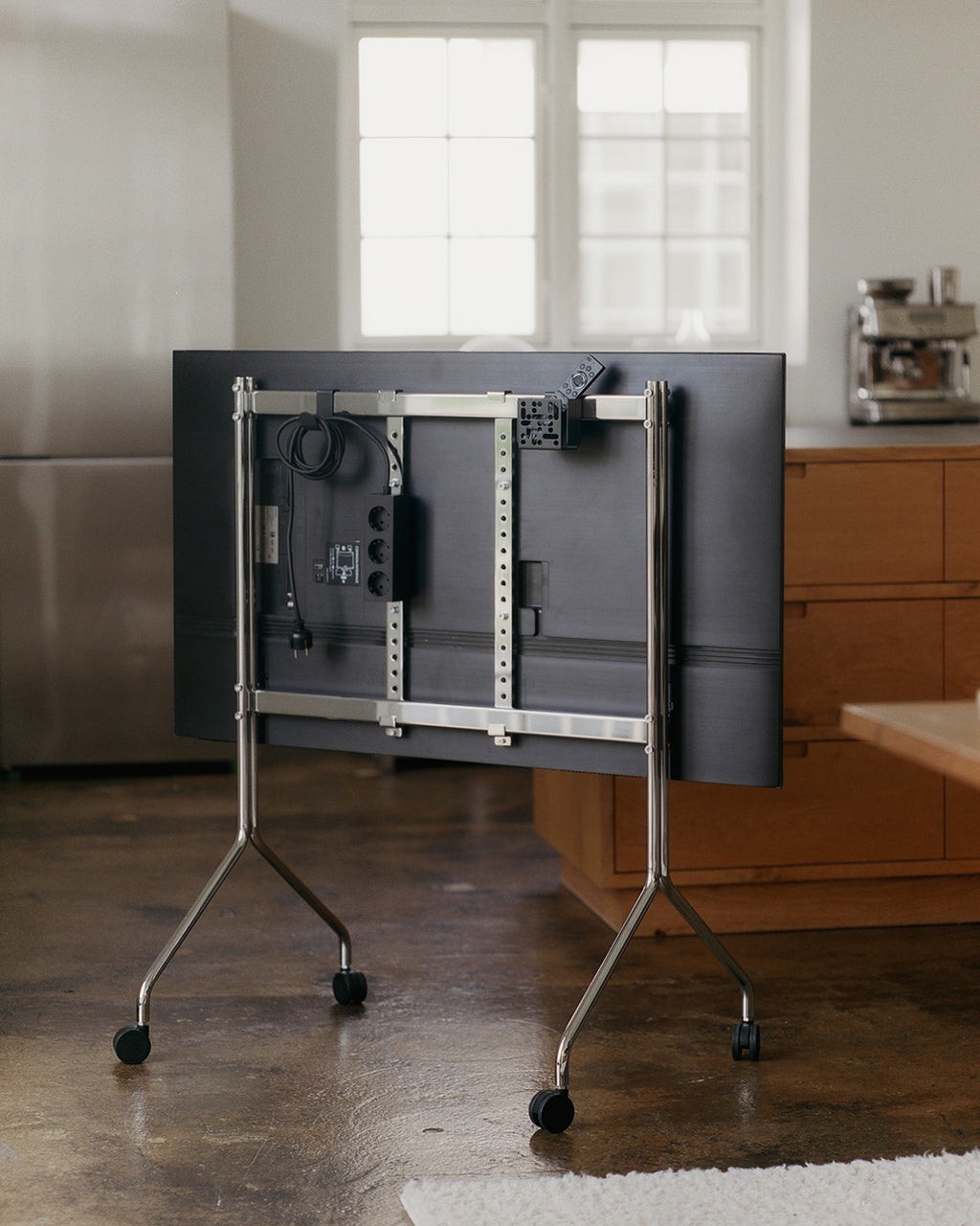 Moon in Chrome stand with wheels holding a folded-down TV, rear view showing cable management in a bright kitchen