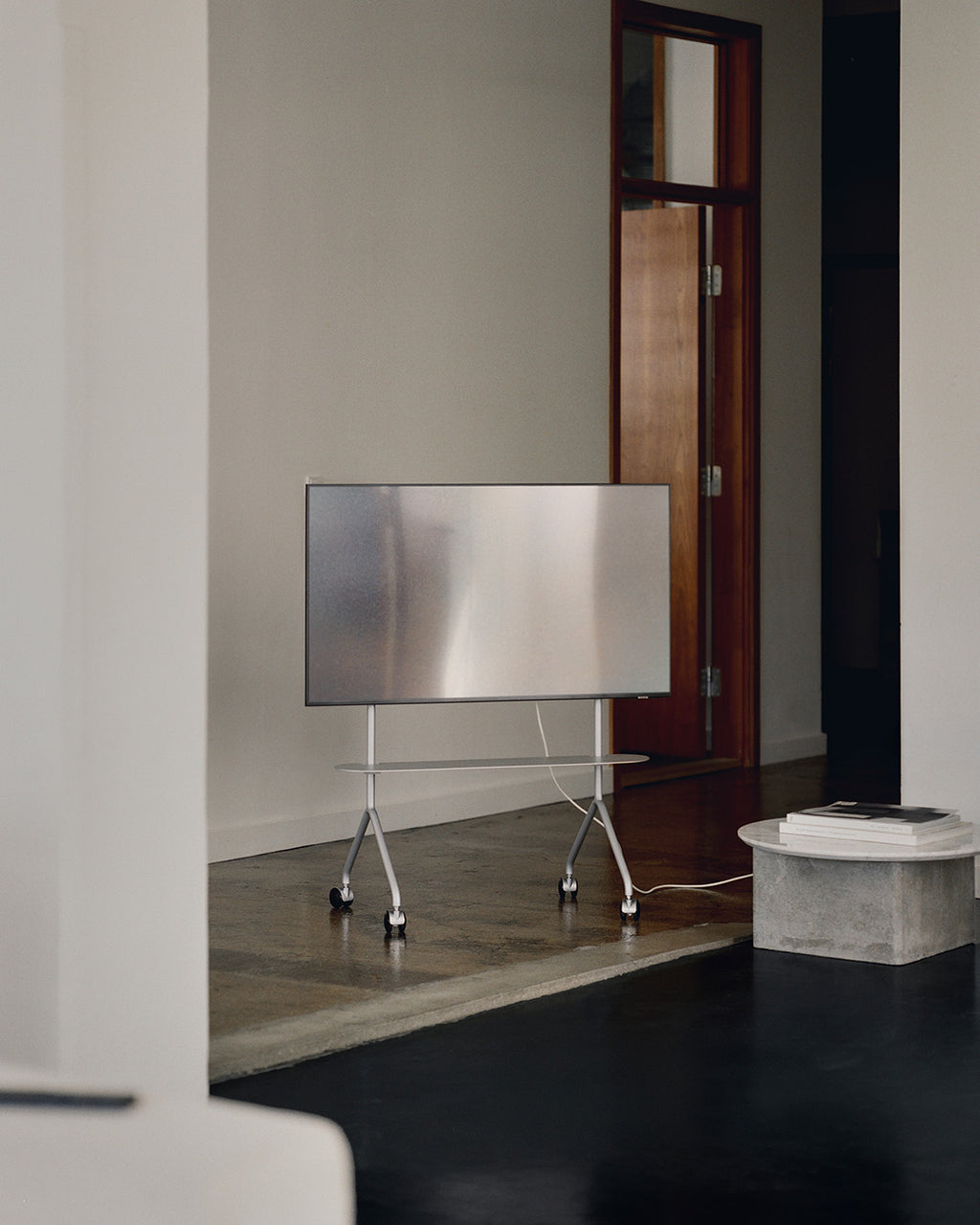 Moon Light in Cloudy Silver rolling TV stand with mounted screen and wheels in a minimal concrete-floored room