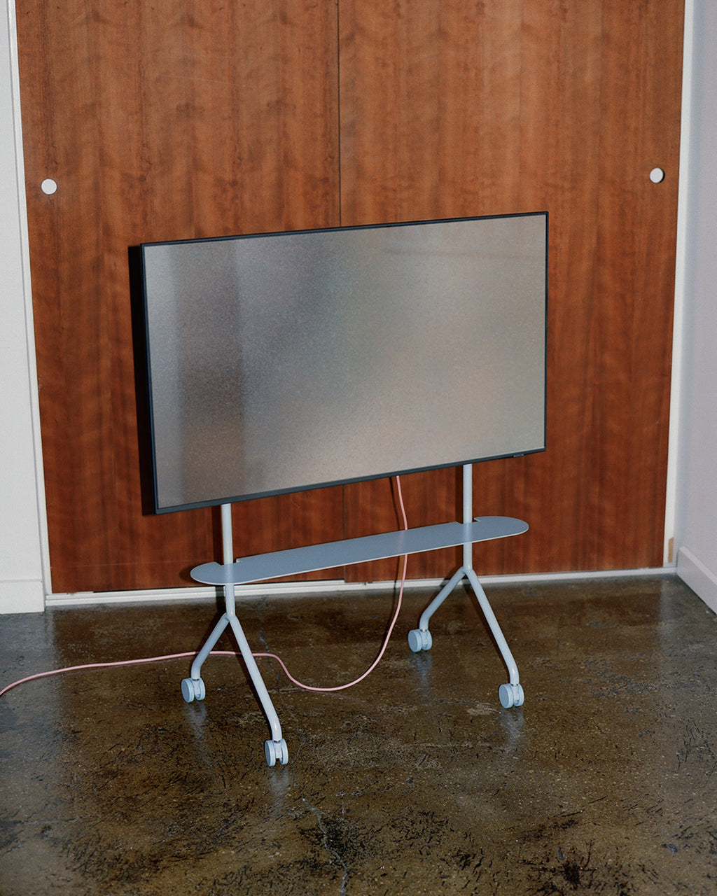 Moon Light Shelf in Powder Blue mounted on a rolling TV stand in a room with wood paneling and concrete floor