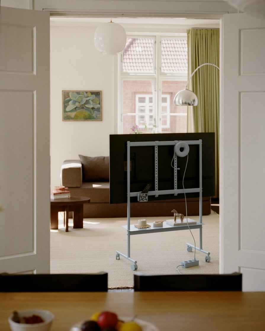 Rover TV stand in Powder Blue on wheels holding a mounted TV, seen from behind in a sunlit living room