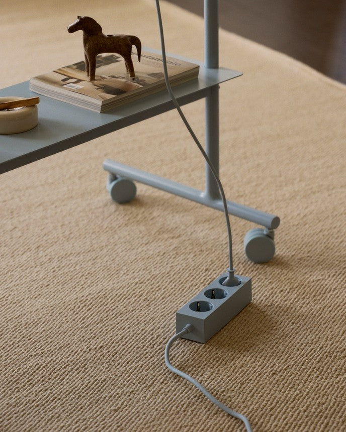Rover stand in Powder Blue on a beige rug, wheeled base beside a side table with a matching power strip and cord